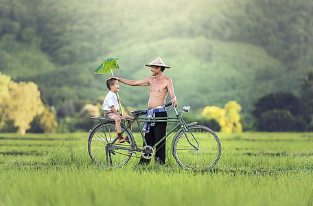 man wearing black pants standing beside green city bicycle with boy wearing white button-up shirt thumbnail