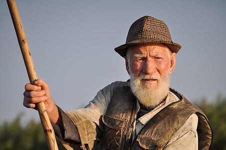 Man Wearing Hat Holding Wooden Rod Under Gray Sky thumbnail