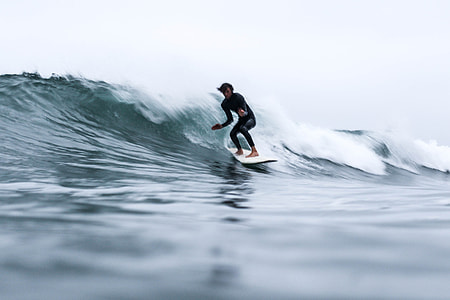 man wearing black wet suit surfing on waves under dark sky during day time thumbnail