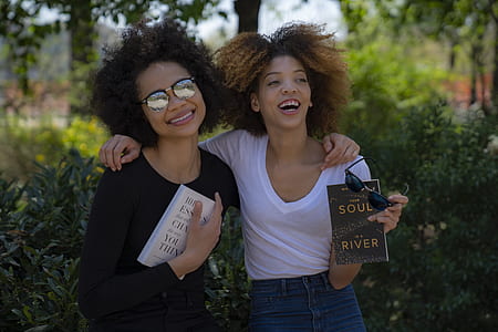 two woman side-by-side holding books in front of plants thumbnail