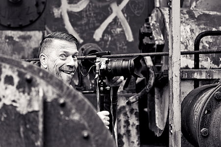 grayscale photo of man smiling in front of DSLR camera thumbnail