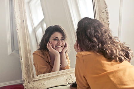 Young woman in Yellow Collared Shirt looking herself reflection in mirror at home thumbnail