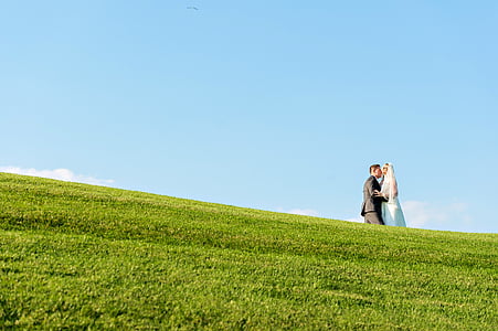 low angle photography of bride and groom on green grass covered hill during daytime thumbnail
