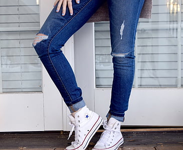 person wearing distressed blue denim fitted jeans and pair of white Converse All Star high top shoes thumbnail