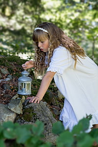 shallow focus photography of girl wearing white dress holding silver-colored kerosene lamp on her right hand during daytime thumbnail