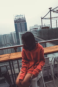 Photograph of Woman Wearing Red Pullover Hoodie Jacket Sitting on White Barstool thumbnail