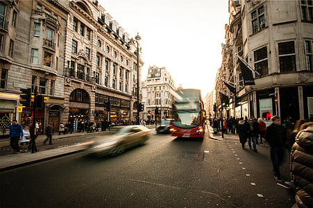 time lapse photography of bus on asphalt road between buildings under blue sky thumbnail