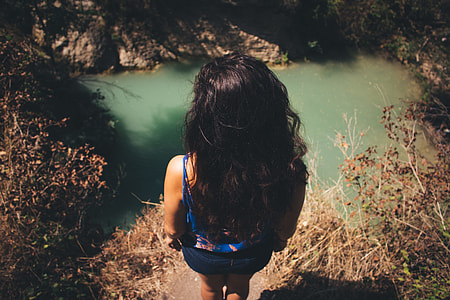 woman standing on cliff facing body of water thumbnail