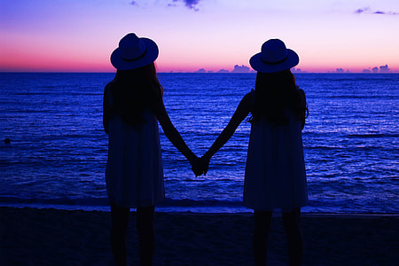 two woman holding beside sea shore thumbnail