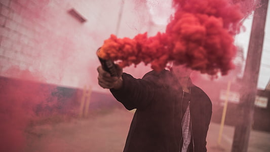 person standing beside wall while holding red smoke during daytime thumbnail