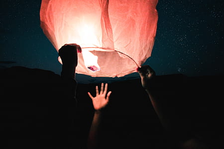 silhouette photo of three hands holding a paper lantern thumbnail