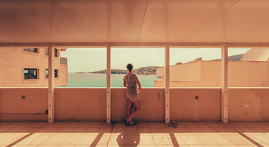 woman standing on white floor tiles in brown concrete building near body of water during daytime thumbnail