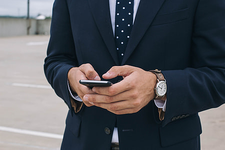 man in  blue suit jacket  and blue necktie holding smartphone during daytime thumbnail