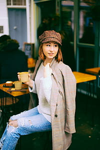 Woman Wearing Brown Coat Holding Cup Sitting on Chair thumbnail