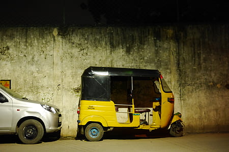 yellow and black auto rickshaw parked by gray concrete wall thumbnail