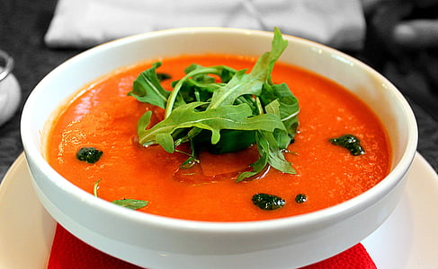 orange soup topped with green leaves in round white ceramic bowl closeup photography thumbnail
