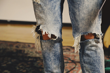 person wearing distressed blue denim jeans standing on multicolored floral area rug thumbnail