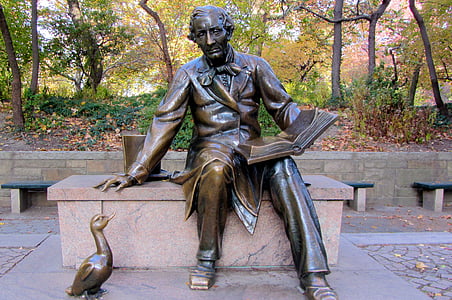man sitting on bench with book on hand beside duck statue thumbnail