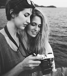 grayscale photo of woman holding camera beside woman thumbnail