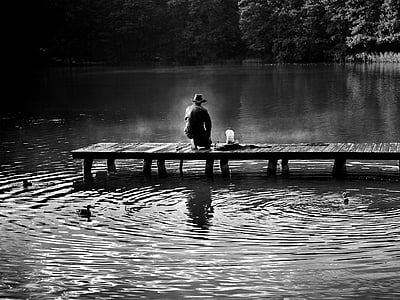 grayscale photo of man sitting down the dock thumbnail