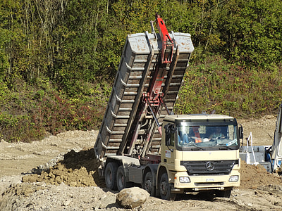white Mercedes-Benz dump truck dumping gravel near trees thumbnail