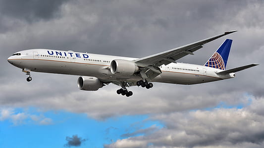 white and blue United airplane flying under gray sky thumbnail