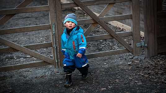 boy wearing blue coat beside brown wooden fence thumbnail