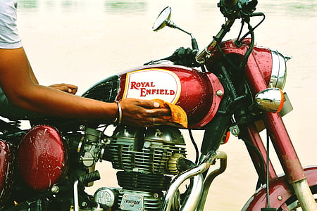 person wiping red and grey Royal Enfield motorcycle thumbnail
