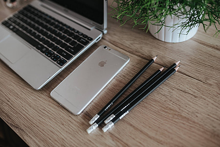 Silver Acer laptop on a wooden desk with a green plant, pencils and an Apple iPhone thumbnail