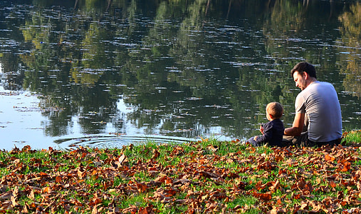 man in gray t-shirt sitting beside boy near body of water thumbnail