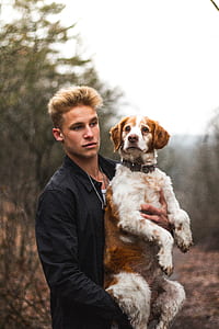 man carrying medium short-coated tan and white dog on selective focus photo thumbnail