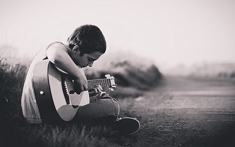 grayscale photography of boy playing guitar thumbnail