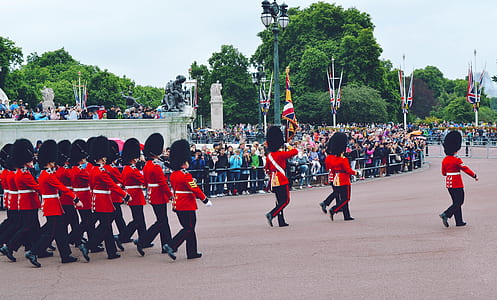 Royal Guards marching on gray concrete pavement surrounded with green trees during daytime thumbnail