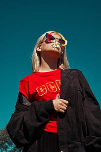 low-angle photo of woman wearing red shirt and black jacket with daisy flower on mouth thumbnail