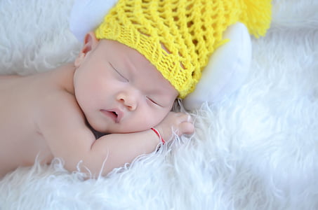 sleeping baby wearing yellow knit cap laying on white fleece textile thumbnail