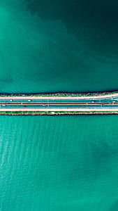 aerial photography of vehicles passing on road surrounded with body of water during daytime thumbnail