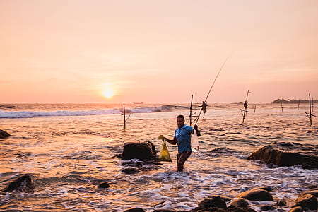 man walking in body of water carrying tote bags and fishing rod thumbnail