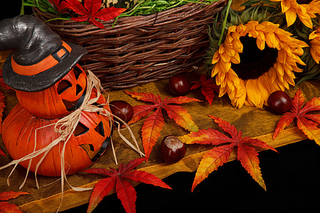 Jack-O-Lantern on table near leaves, basket, and sunflowers thumbnail
