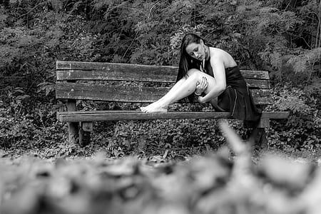 grayscale photography of woman sitting on wooden bench thumbnail