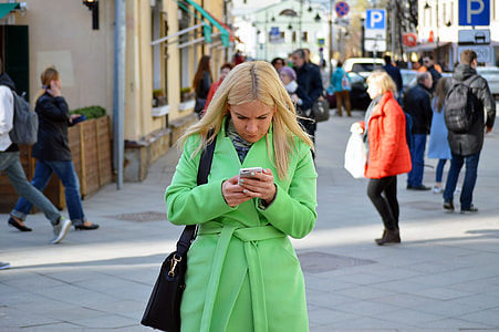 woman in green coat holding phone behind people thumbnail