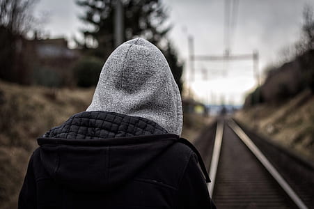 person wearing black and gray jacket standing on train rail during daytime thumbnail