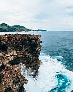 person standing on cliff near body of water thumbnail