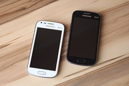 two white and black Samsung Android smartphones on brown wooden surface thumbnail