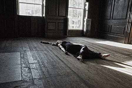 grayscale photo of person lying on brown floor inside house thumbnail