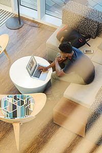 man in blue shirt and brown pants holding MacBook sitting on gray fabric sectional sofa thumbnail