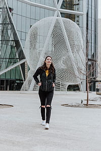 woman walking on gray concrete ground near head statue besided curtained wall building during daytime thumbnail