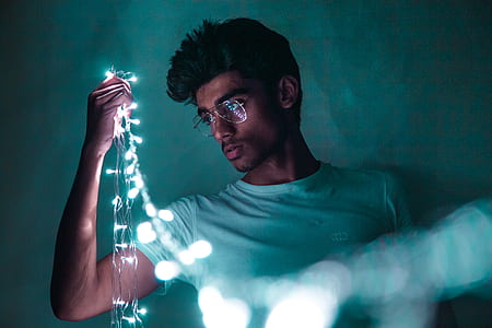 man wearing white crew-neck shirt holding green string lights thumbnail