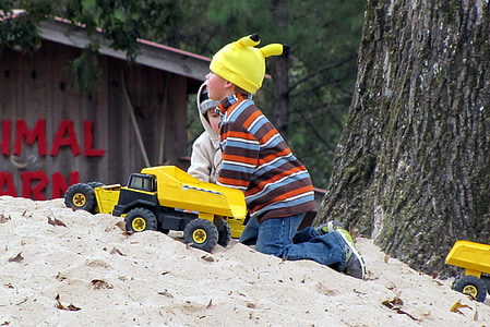 toddler boy kneeling on sand near yellow and black dump truck toy thumbnail