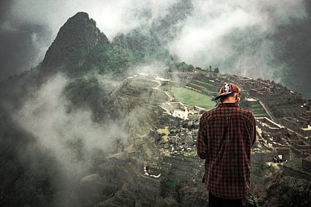 man in red and gray plaid dress shirt and cap standing on top of mountain thumbnail
