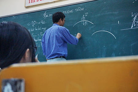 person in blue dress shirt holding chalk while writing on chalkboard thumbnail
